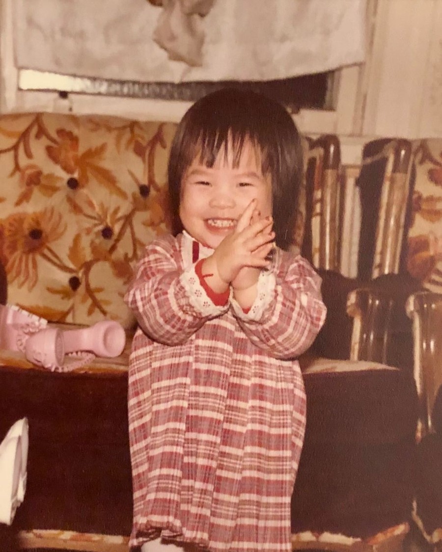 Angela as a little girl, mid-clap, in a red plaid dress